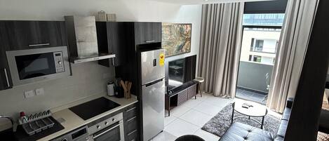 A modern kitchen with a microwave, stove, and refrigerator. There is a dining area with a table and chairs, and a view of the outside through large windows.