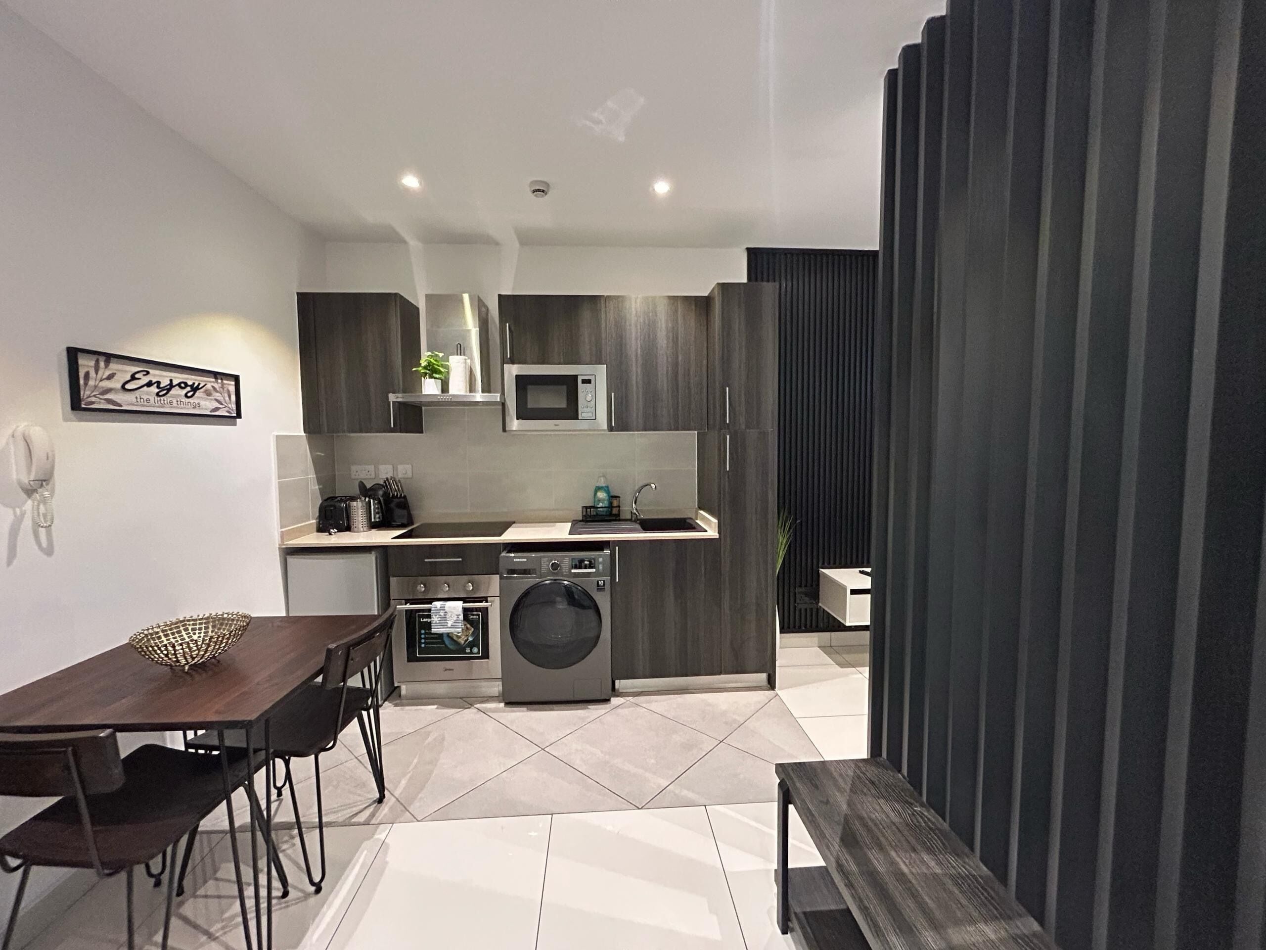 A modern kitchen with a microwave, oven, and sink. There is a dining table with chairs and a bench.