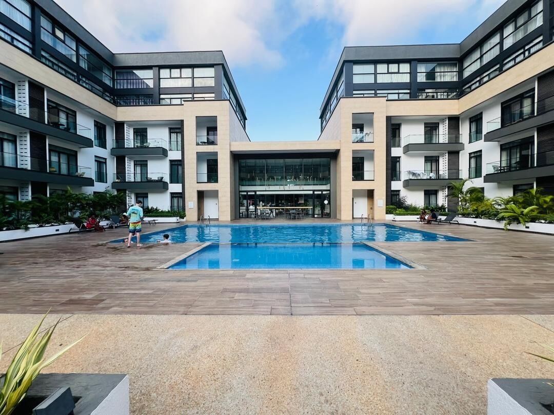 Un bâtiment moderne doté d’une piscine centrale, de nombreux balcons et d’une entrée abritée.