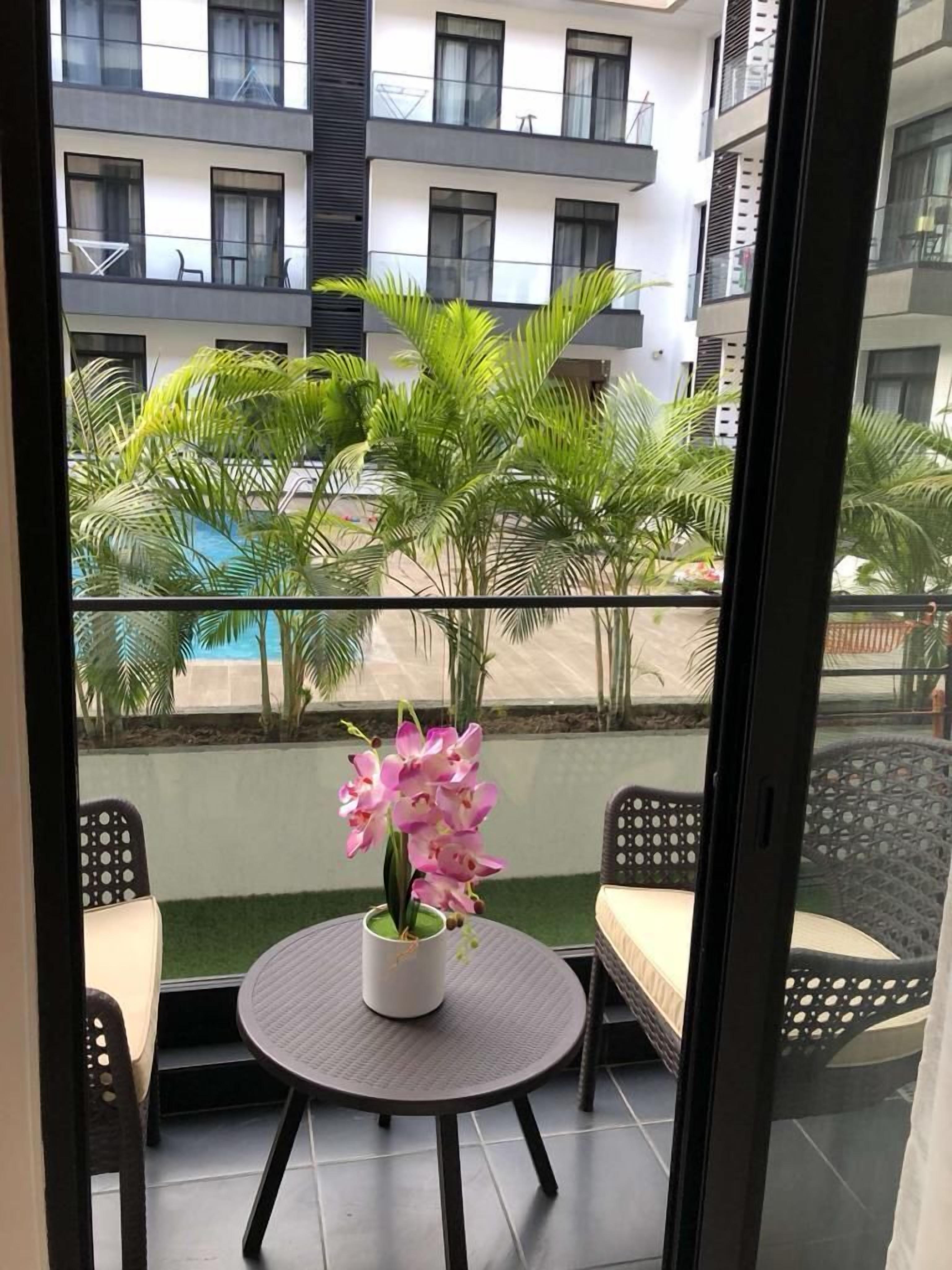 A balcony with a round table, two chairs, and a potted orchid.