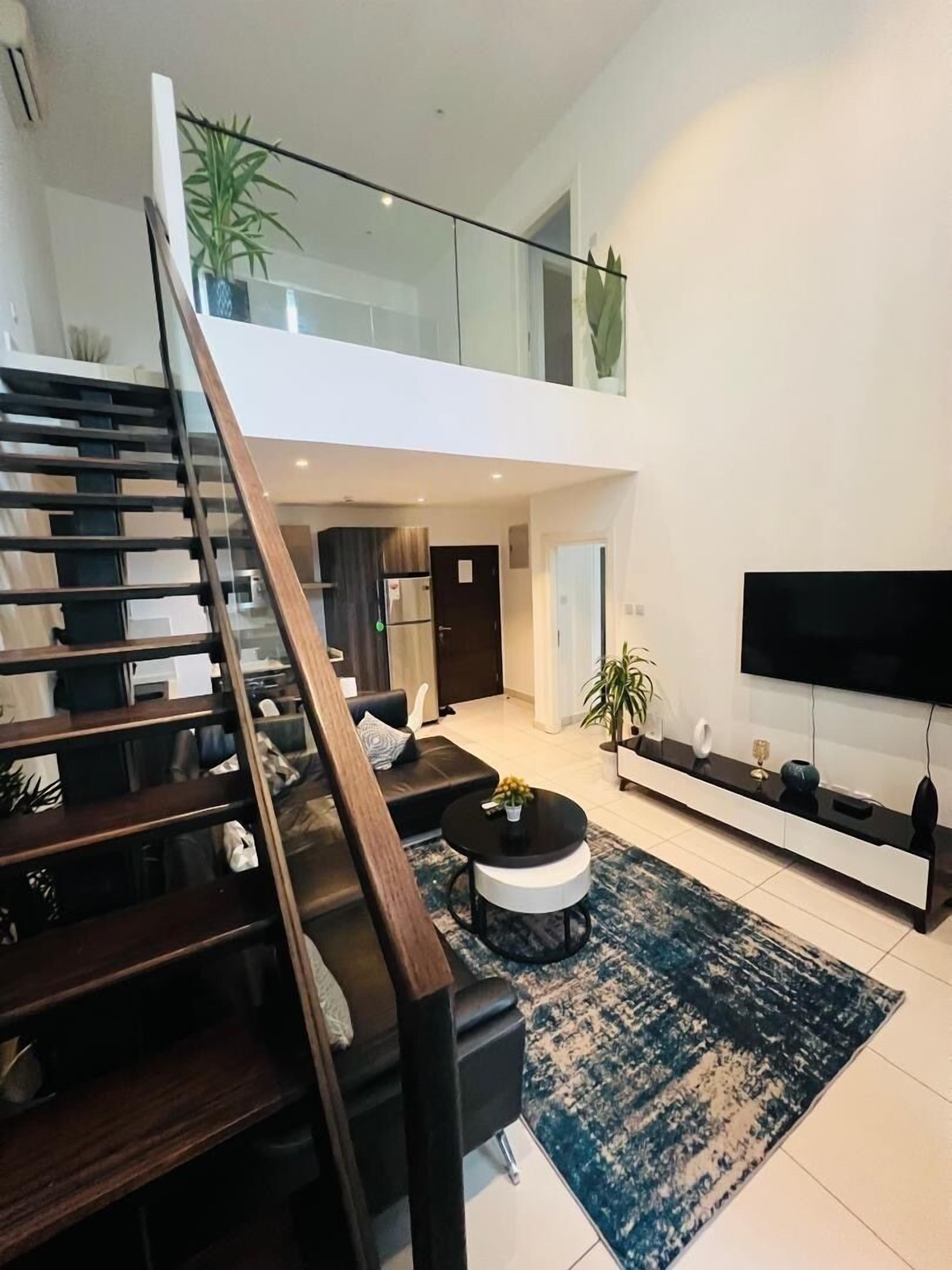 A modern living room with a staircase, a flat-screen TV, and a large plant.