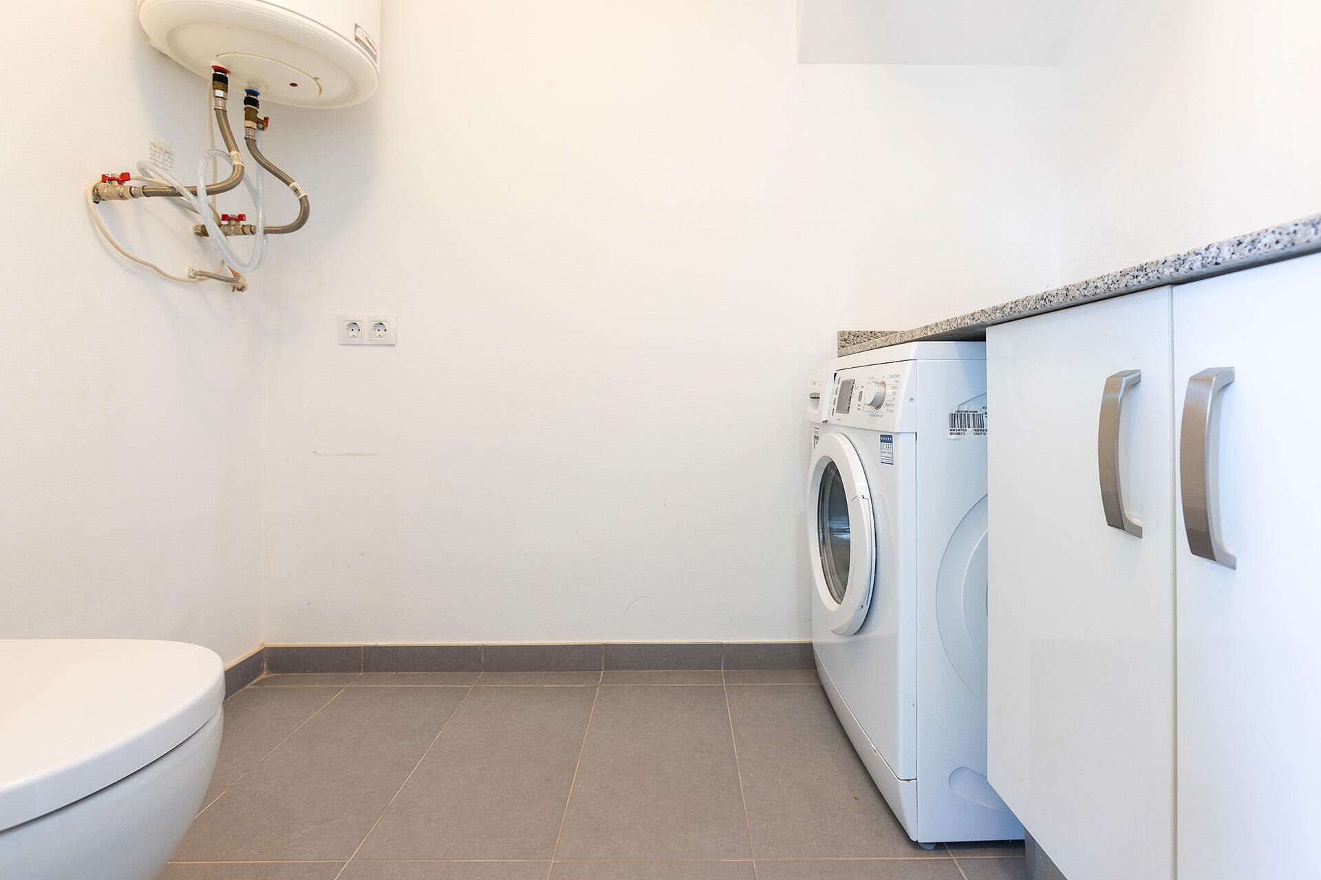 A compact bathroom with a toilet, a washing machine, and a built-in sink with a faucet.