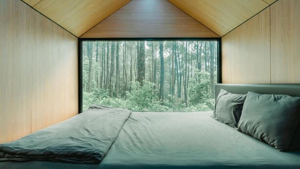 Un dormitorio con un ventanal, una cama y vistas a un bosque.