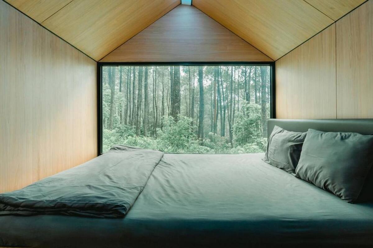 A bedroom with a large window, a bed, and a view of a forest.