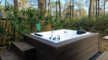 Uma banheira de hidromassagem em área arborizada, com deck de madeira e cerca de bambu.
