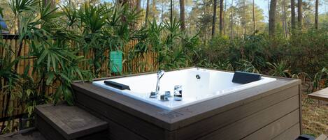 Un bain à remous situé dans un espace boisé, avec une terrasse en bois et une clôture en bambou.
