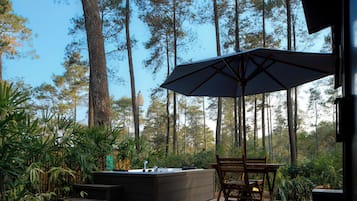 Um pátio externo com mesa e cadeiras de madeira, um grande guarda-sol e uma churrasqueira fixa.