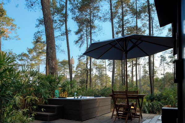 An outdoor patio with a wooden table and chairs, a large umbrella, and a built-in barbecue grill. - Bobocabin Cikole (Lembang)