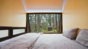 Ein Schlafzimmer mit großem Fenster, einem Bett und Blick auf einen Wald.
