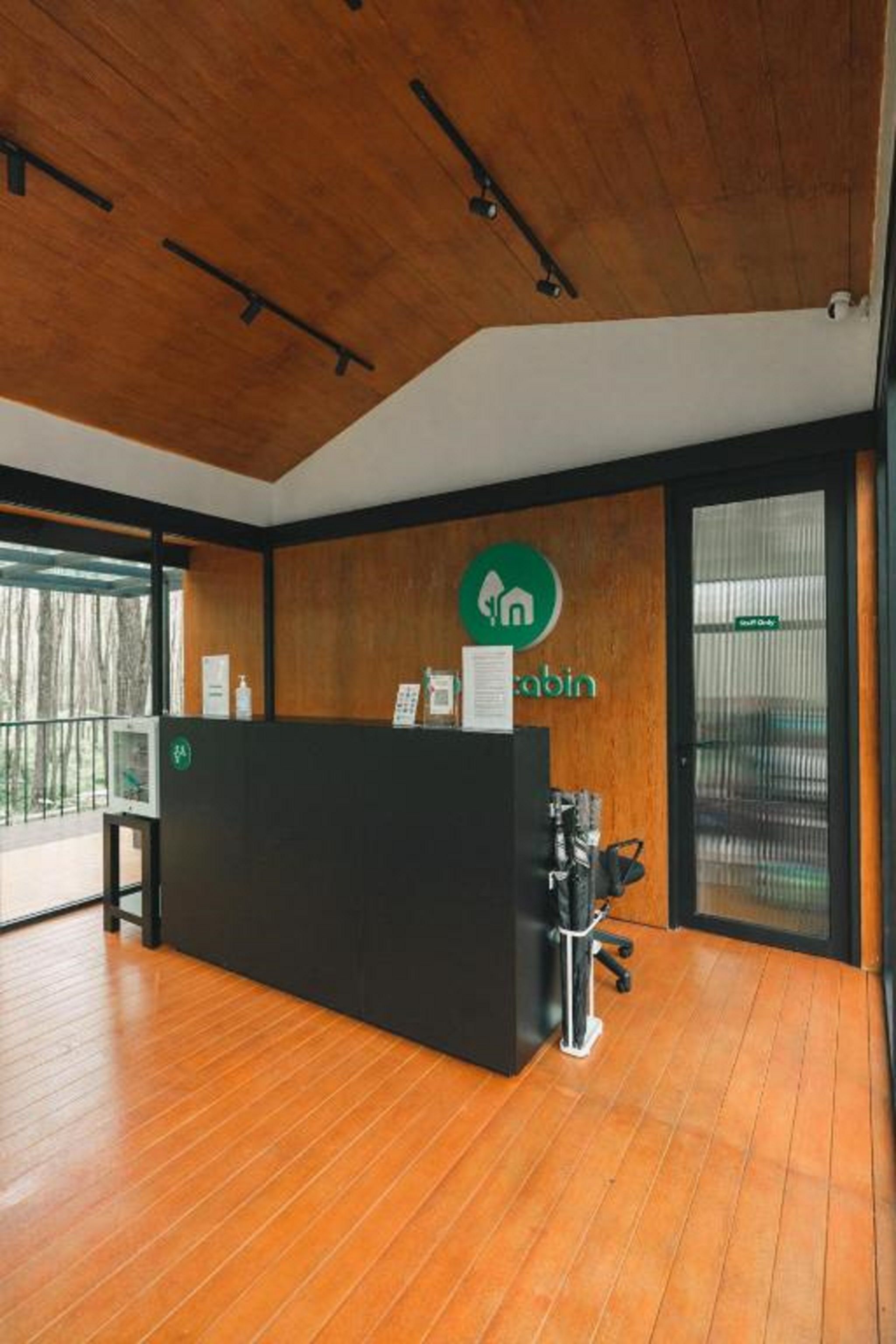 Balcão de recepção com piso de madeira, bancada preta e logotipo verde na parede.