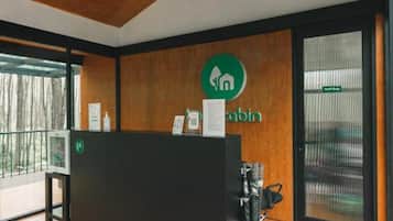 Balcão de recepção com piso de madeira, bancada preta e logotipo verde na parede.