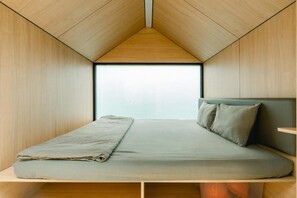 A compact, triangular room with a bed, pillows, and a window. - Bobocabin Cikole (Lembang)