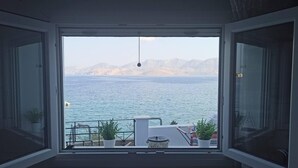 Ein Zimmer mit großem Fenster und Blick auf ein Gewässer und ferne Berge.