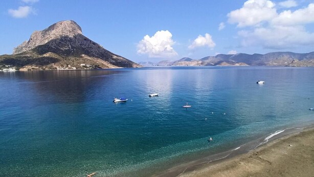 Eine Küstenlandschaft mit einem Berg, klarem blauen Wasser und einem Sandstrand.