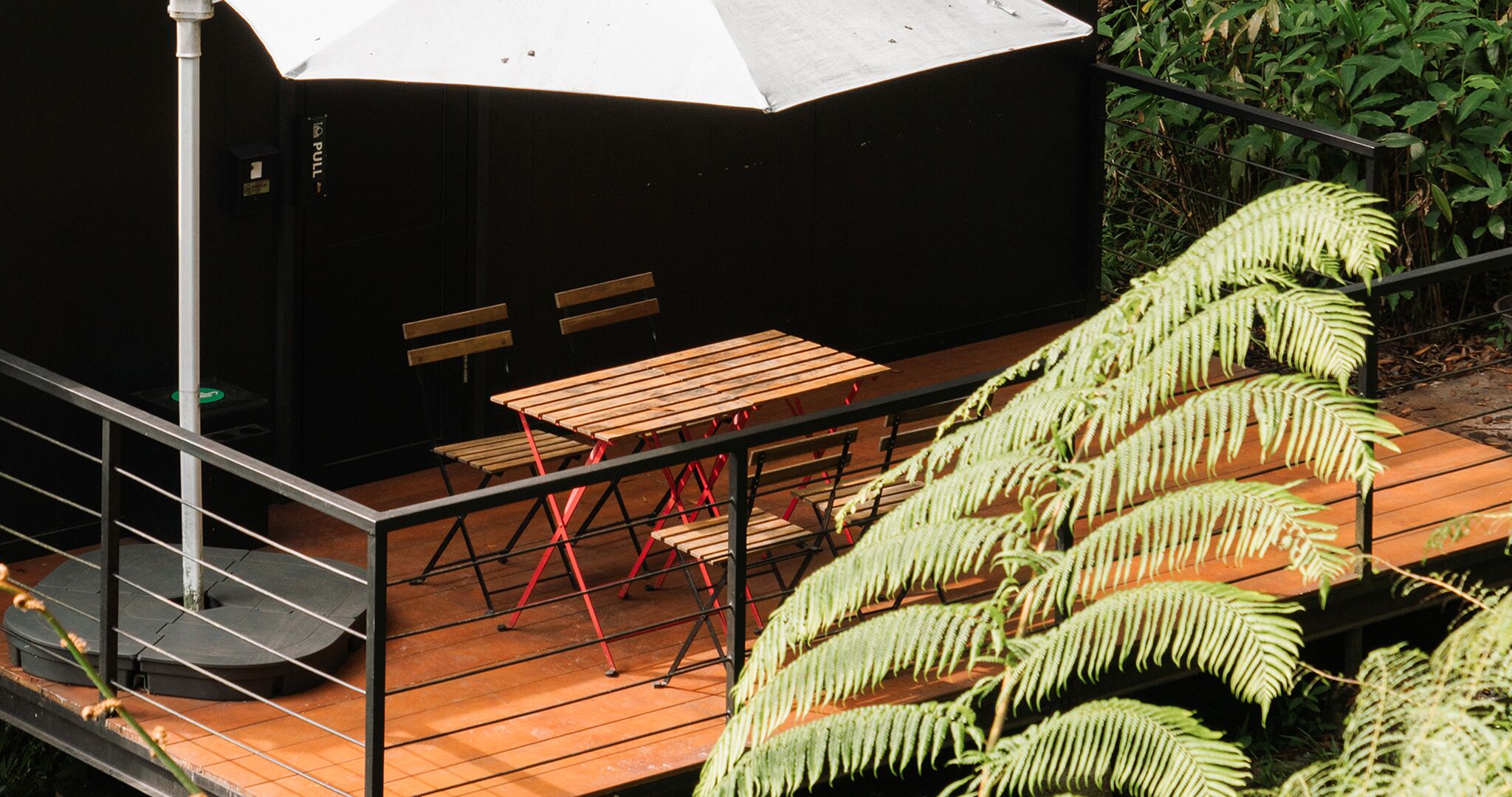 A wooden deck with a table and benches, surrounded by ferns.