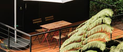 A wooden deck with a table and benches, surrounded by ferns.