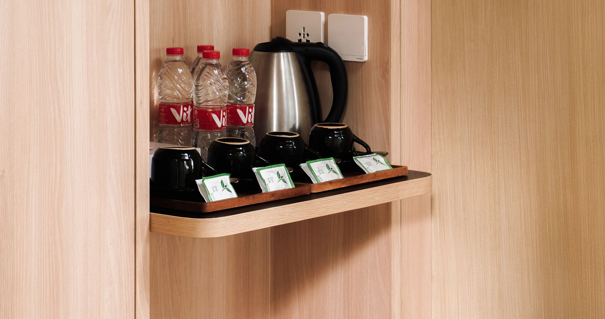 Une étagère en bois avec une bouilloire, des tasses à café et des bouteilles d’eau.