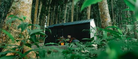 A cabin in a forest with a metal roof and a wooden deck.