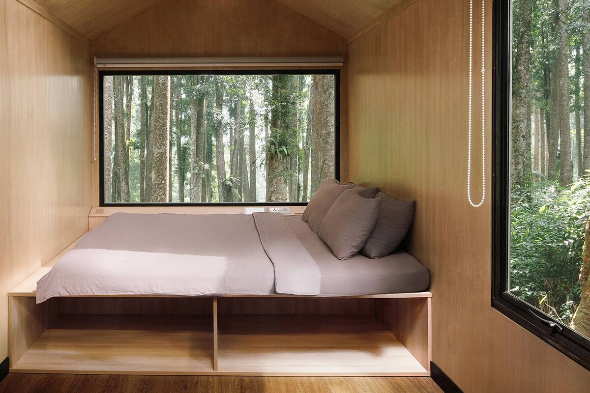 A compact bedroom with a bed, a window, and a view of a forest.