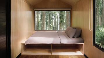A compact bedroom with a bed, a window, and a view of a forest.