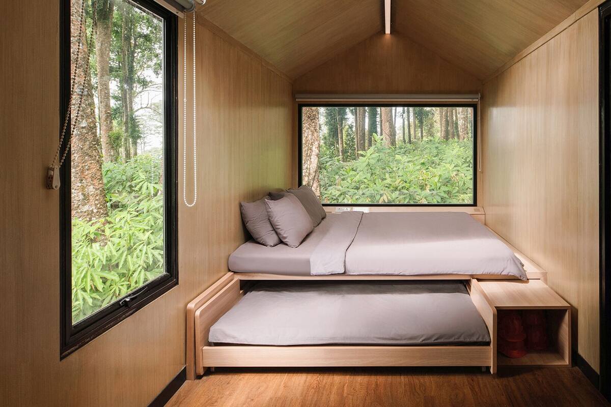 A compact, wooden interior with a bed, a small table, and a window offering a forest view.