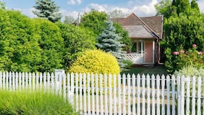 A house with a white picket fence, surrounded by lush greenery and a clear blue sky.