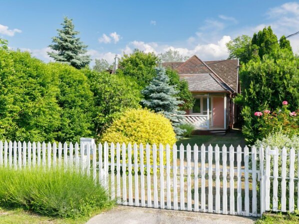 A house with a white picket fence, surrounded by lush greenery and trees.