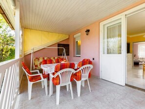 A covered patio with a table and chairs, a door leading to a bedroom, and a view of the outdoors.