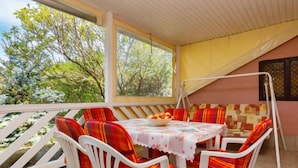 A covered outdoor seating area with a table and chairs, surrounded by a white fence and trees.