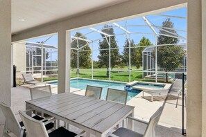 A covered outdoor area with a pool, lounge chairs, and a table.