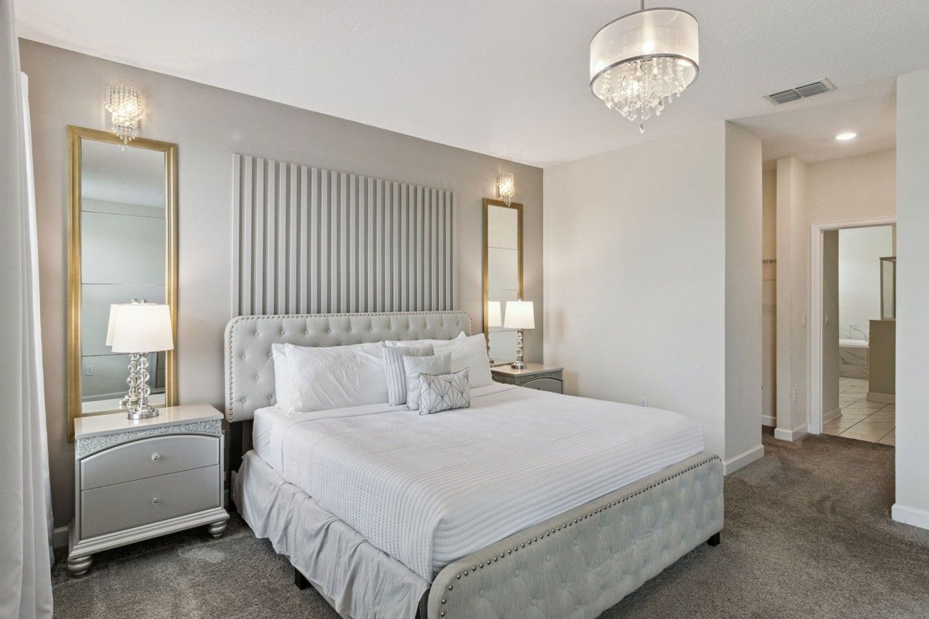 Une chambre d’hôtel avec un grand lit, deux tables de chevet, un lustre et un miroir.