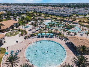 Un resort con una grande piscina centrale circondata da aree relax e palme.