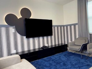 A modern living room with a flat-screen TV mounted on a wall with a Mickey Mouse silhouette, a blue carpet, and two armchairs.
