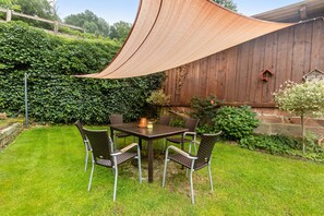 Eine Terrasse mit Tisch und Stühlen, umgeben von einem Holzzaun und viel Grün.