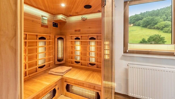 A sauna with wooden benches, a bench with a towel, and a window with a view of a green landscape.