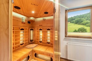 Un sauna avec des bancs en bois, un banc avec une serviette, et une fenêtre donnant sur un paysage verdoyant.