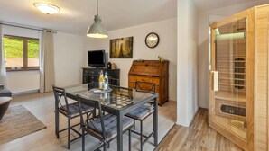 A dining area with a glass table and chairs, a wooden cabinet, a television, and a clock on the wall.