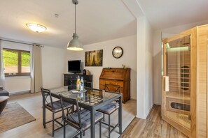 Un coin repas avec une table et des chaises en verre, un meuble en bois, un téléviseur et une horloge au mur.