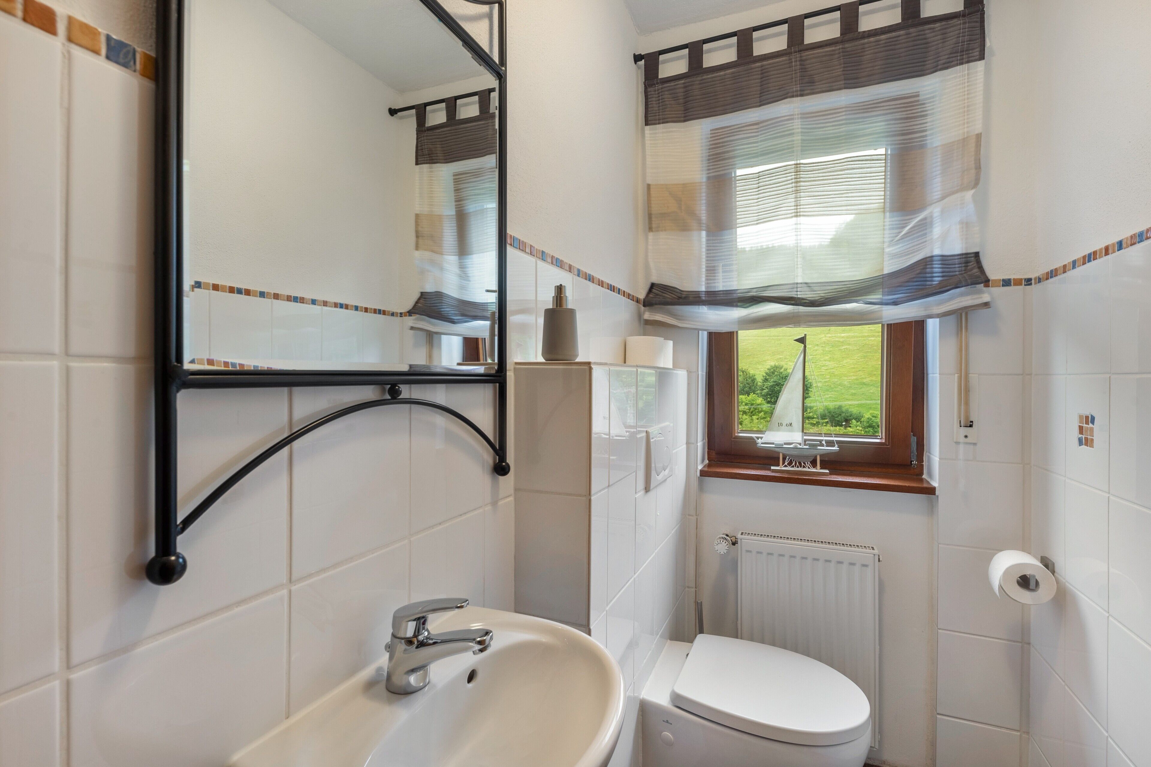 A bathroom with a white sink, a toilet, a mirror, and a window with curtains.