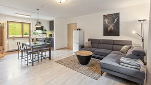 A modern living room with a grey sofa, a dining table with chairs, a kitchen in the background, and a large deer artwork on the wall.