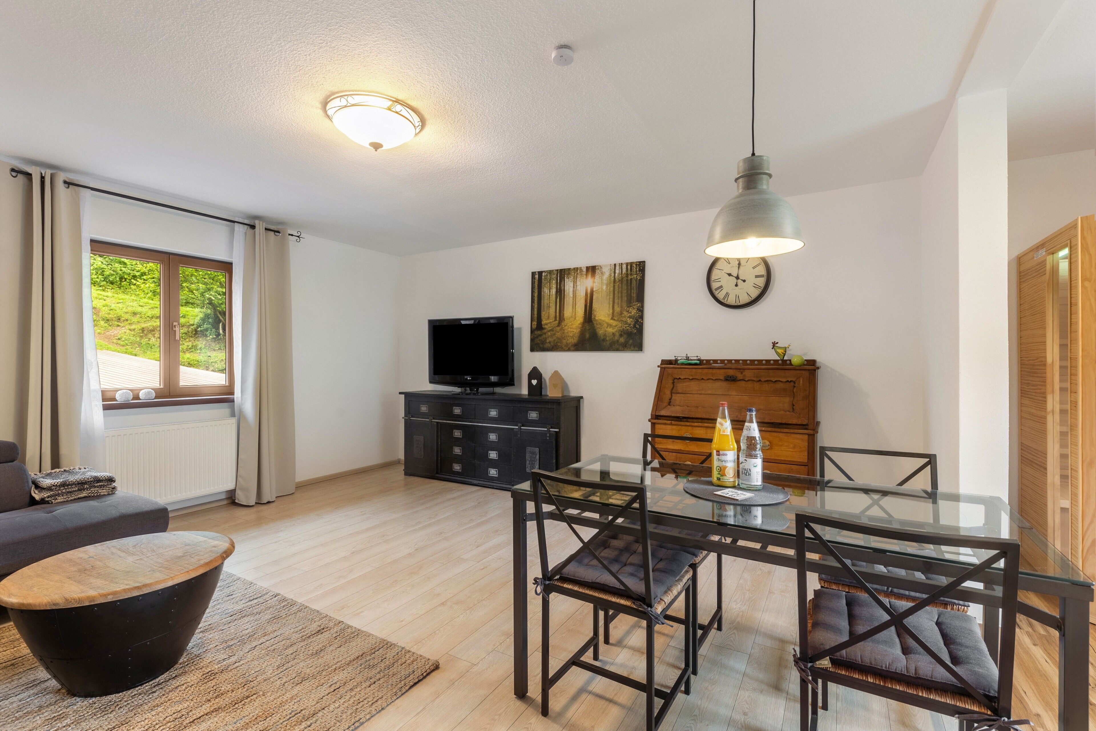 A modern living room with a glass dining table, black chairs, a sofa, a television, and a wooden cabinet.