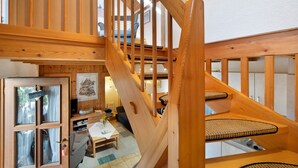 A wooden staircase leading to a loft bedroom with a view of the outdoors.