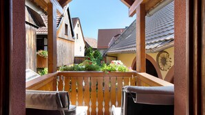 A wooden balcony with a view of traditional buildings, a clock, and a flower box.