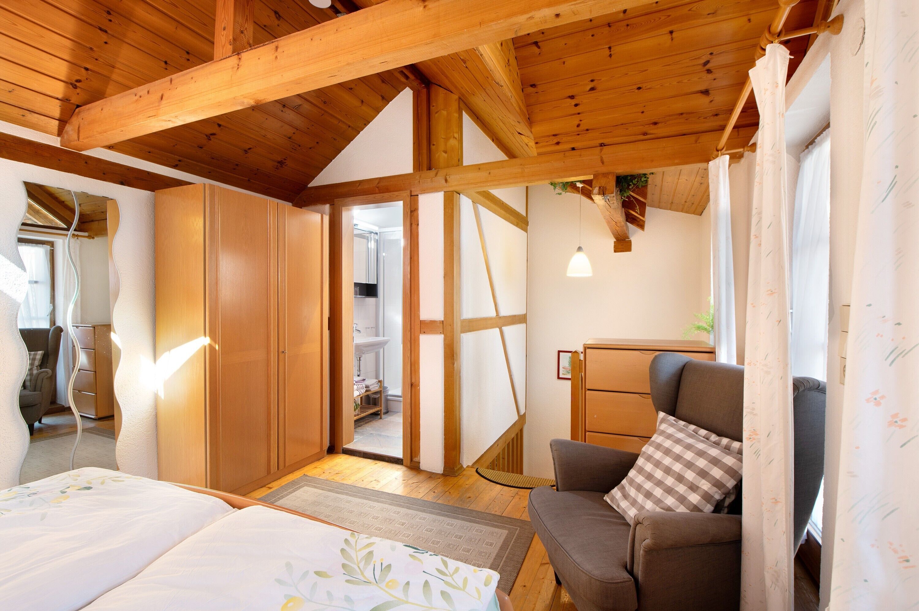 Una stanza con soffitto in legno, un letto, una poltrona e vista su un'altra stanza.