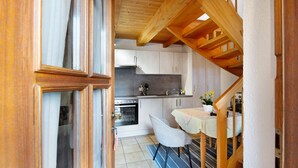 A narrow kitchen with wooden beams, a dining area with a table and chairs, and a staircase leading to another level.
