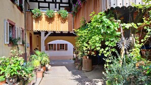 A courtyard with potted plants, a wooden pergola, and a building with a white facade and arched windows.
