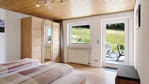 Een slaapkamer met een bed, een houten garderobe en uitzicht op de omgeving door een deur.