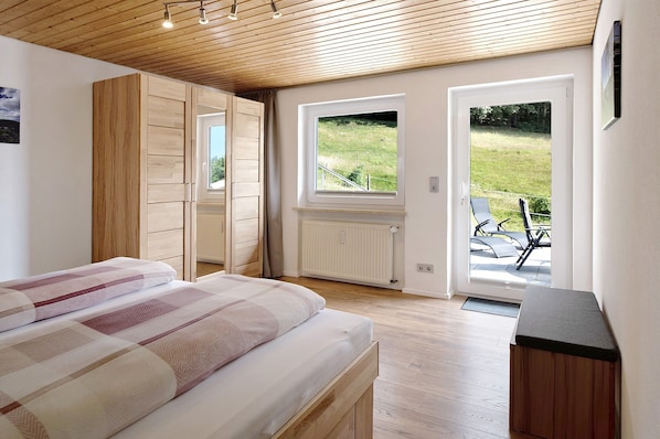 A bedroom with a bed, wooden wardrobe, and a view of the outdoors through a door.