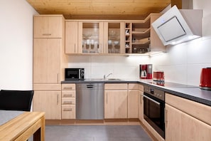 A kitchen with wooden cabinets, a dishwasher, a microwave, a coffee maker, and a red kettle.