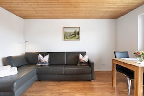 A modern living room with a leather sofa, a wooden dining table, and a painting on the wall.
